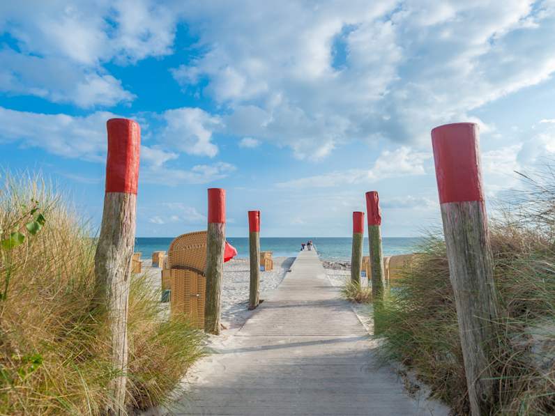 Ein Holzsteg führt zum Meer an einem Strand mit Strandkörben